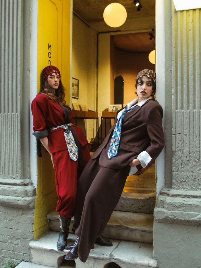 services-04 Two stylish women pose in vibrant suits and ties on a staircase, exuding modern fashion.